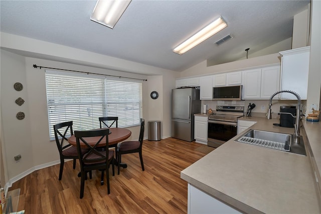 kitchen with sink, vaulted ceiling, light wood-type flooring, stainless steel appliances, and white cabinets