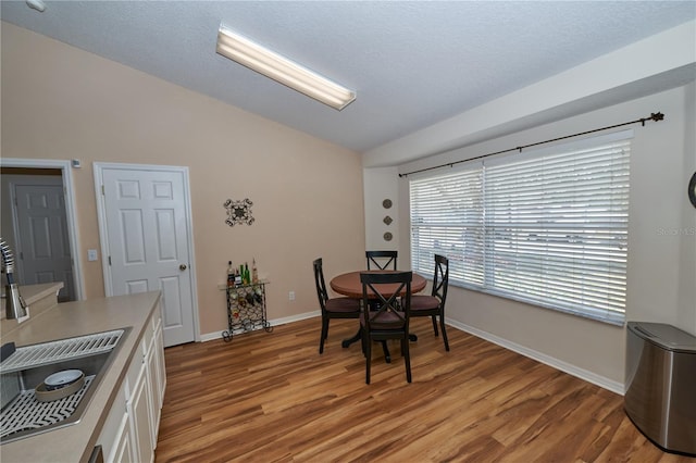 dining area featuring lofted ceiling, sink, hardwood / wood-style floors, and a textured ceiling