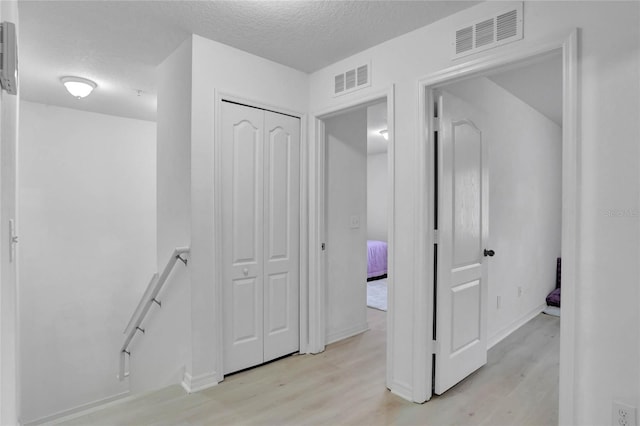 hallway with light hardwood / wood-style floors and a textured ceiling