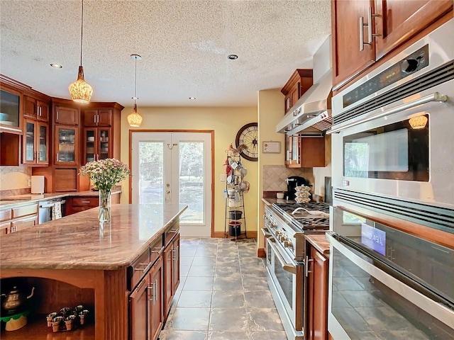 kitchen with appliances with stainless steel finishes, light stone countertops, pendant lighting, range hood, and backsplash