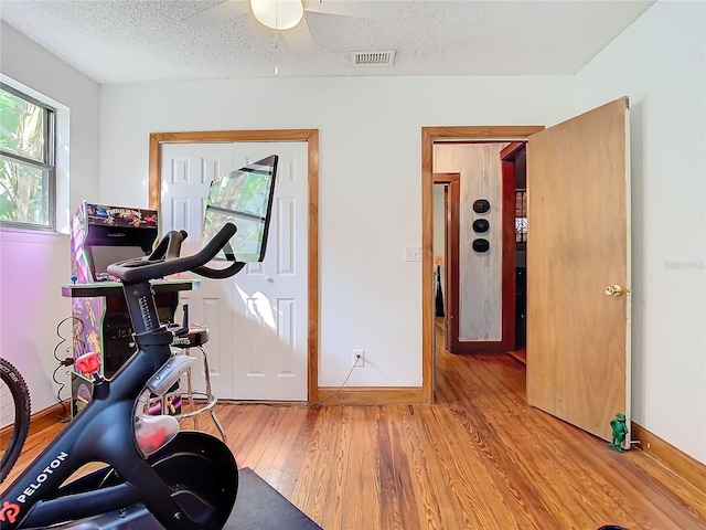 workout room with ceiling fan, wood-type flooring, and a textured ceiling