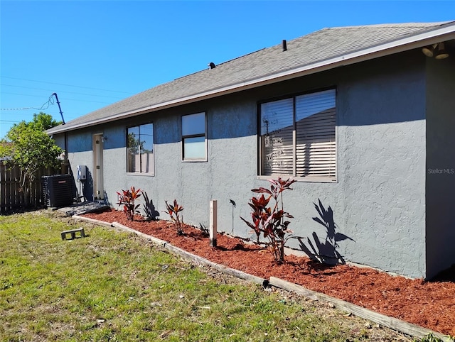 view of property exterior featuring a yard, central air condition unit, stucco siding, and fence