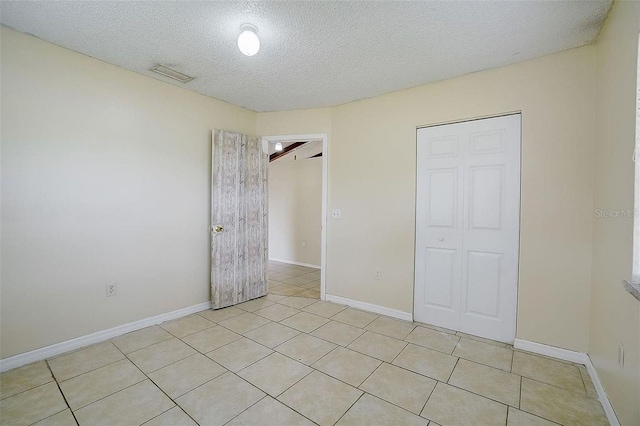unfurnished bedroom featuring light tile patterned floors, a closet, a textured ceiling, visible vents, and baseboards