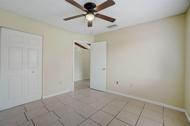unfurnished bedroom with a ceiling fan, a textured ceiling, light tile patterned floors, baseboards, and visible vents