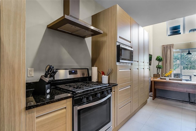 kitchen featuring light tile patterned flooring, appliances with stainless steel finishes, wall chimney range hood, and dark stone counters