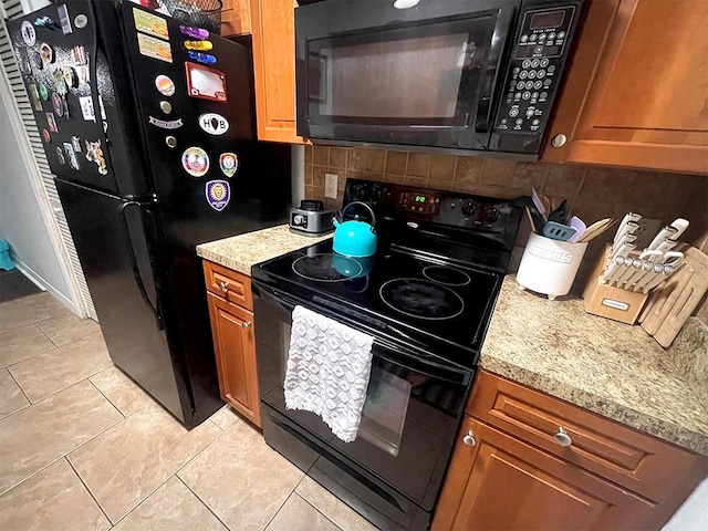 kitchen featuring tasteful backsplash, light stone countertops, light tile patterned floors, and black appliances