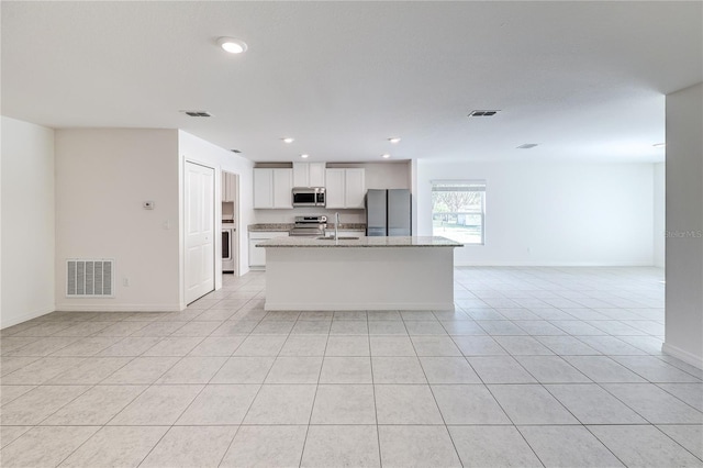 kitchen with sink, appliances with stainless steel finishes, light stone countertops, a kitchen island with sink, and white cabinets