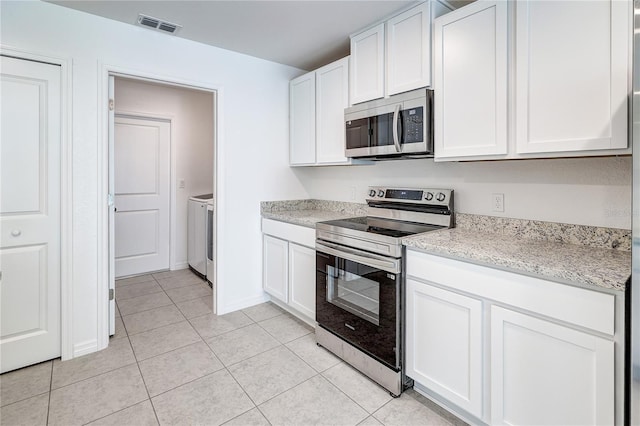 kitchen with appliances with stainless steel finishes, washer and dryer, light tile patterned floors, and white cabinets