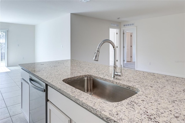 kitchen with light tile patterned flooring, sink, white cabinetry, dishwasher, and light stone countertops