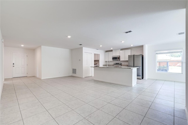 kitchen featuring light tile patterned flooring, white cabinetry, light stone counters, appliances with stainless steel finishes, and an island with sink