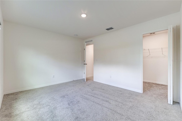 unfurnished bedroom with a walk in closet, light colored carpet, and a closet