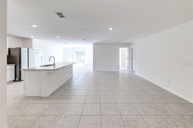 kitchen with sink, light tile patterned floors, stainless steel refrigerator, a kitchen island with sink, and white cabinets