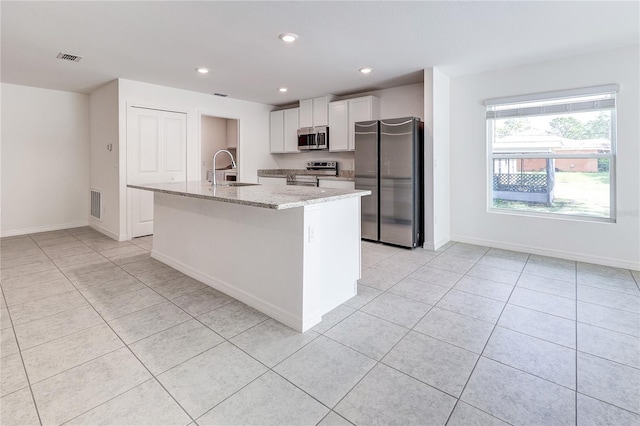 kitchen with sink, white cabinetry, stainless steel appliances, light stone countertops, and an island with sink