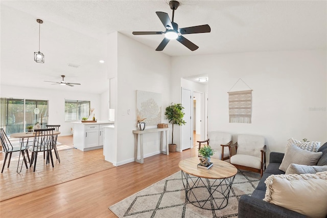 living room featuring lofted ceiling, a textured ceiling, light hardwood / wood-style floors, and ceiling fan