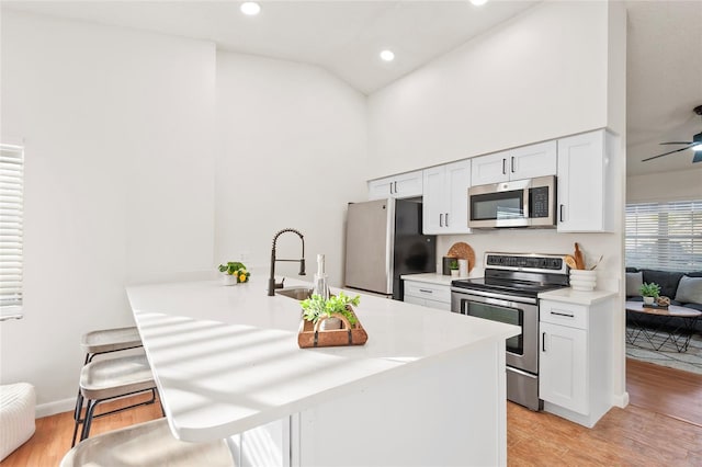 kitchen with stainless steel appliances, white cabinetry, light hardwood / wood-style flooring, and kitchen peninsula