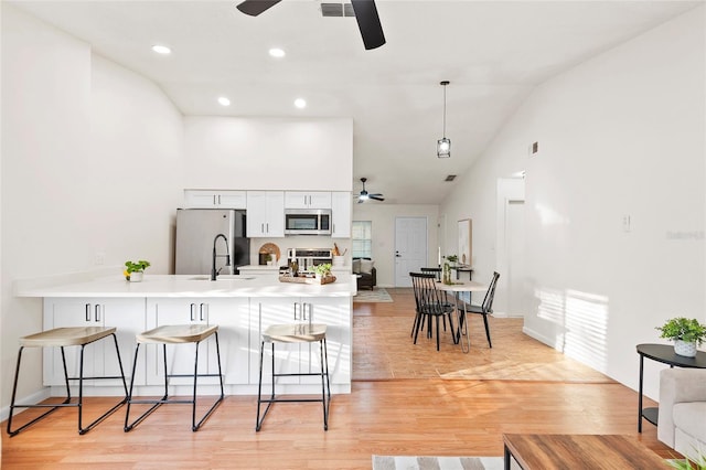 kitchen featuring white cabinetry, a kitchen breakfast bar, kitchen peninsula, stainless steel appliances, and light hardwood / wood-style flooring