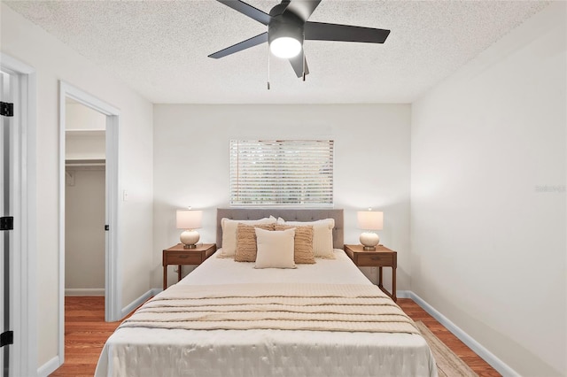 bedroom with a walk in closet, light hardwood / wood-style flooring, a textured ceiling, a closet, and ceiling fan