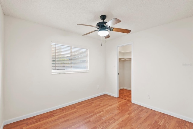 unfurnished bedroom featuring light wood-type flooring, a walk in closet, ceiling fan, a textured ceiling, and a closet