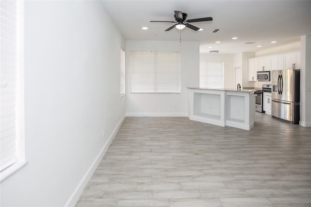 kitchen with white cabinetry, light stone counters, light wood-type flooring, appliances with stainless steel finishes, and ceiling fan