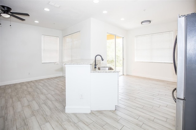 kitchen with ceiling fan, sink, light stone counters, and stainless steel refrigerator