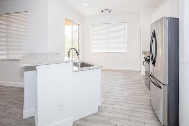 kitchen featuring stainless steel appliances, white cabinetry, light stone countertops, and sink