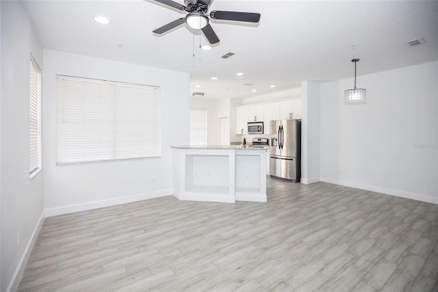 unfurnished living room featuring ceiling fan with notable chandelier and light hardwood / wood-style flooring