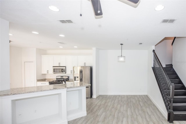 kitchen featuring pendant lighting, appliances with stainless steel finishes, white cabinetry, a center island, and light stone countertops