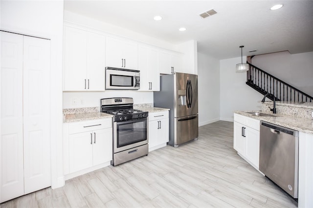 kitchen featuring pendant lighting, sink, appliances with stainless steel finishes, light stone countertops, and white cabinets