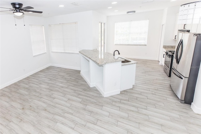 kitchen with appliances with stainless steel finishes, sink, white cabinets, light stone counters, and light wood-type flooring