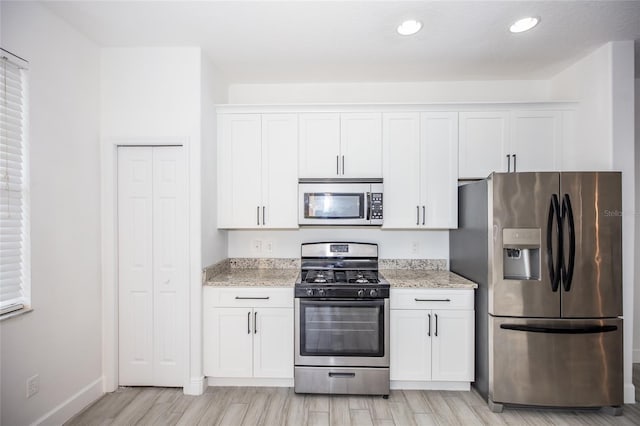 kitchen with white cabinetry, appliances with stainless steel finishes, light stone counters, and light hardwood / wood-style flooring