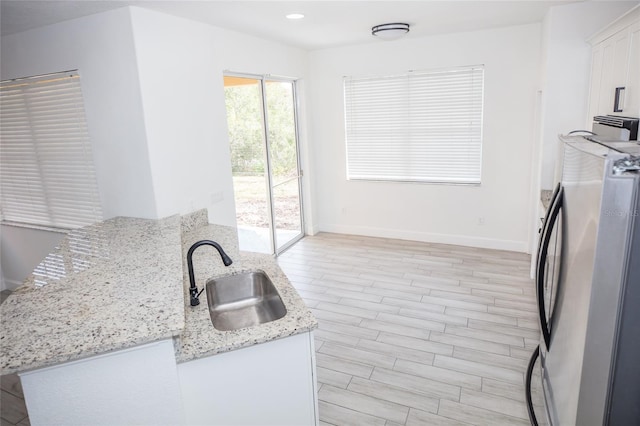 kitchen with sink, white cabinetry, light stone counters, light hardwood / wood-style flooring, and stainless steel refrigerator