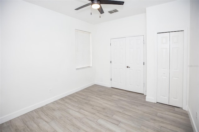 unfurnished bedroom with two closets, ceiling fan, and light wood-type flooring