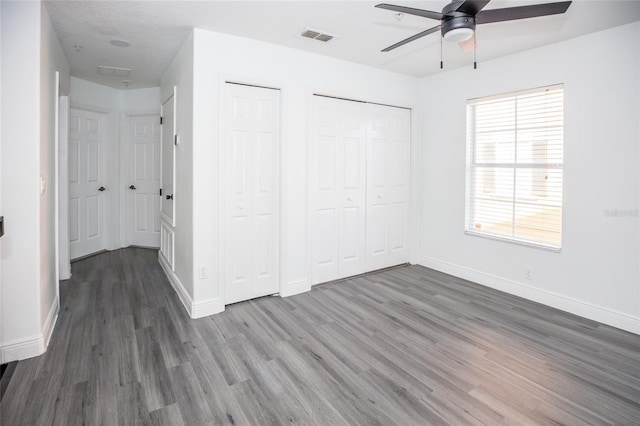 unfurnished bedroom with ceiling fan, two closets, and dark hardwood / wood-style flooring