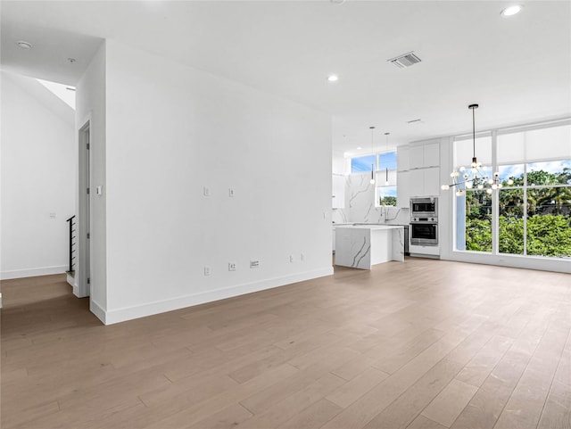 unfurnished living room with a notable chandelier and light hardwood / wood-style flooring