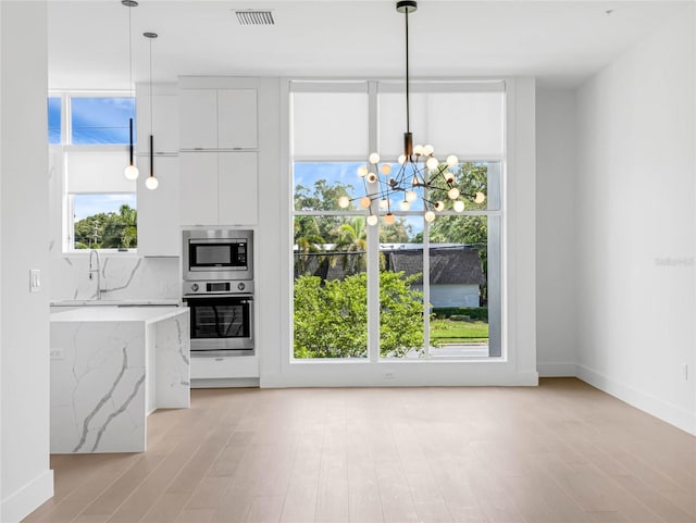 kitchen featuring white cabinetry, hanging light fixtures, light hardwood / wood-style floors, stainless steel appliances, and light stone countertops