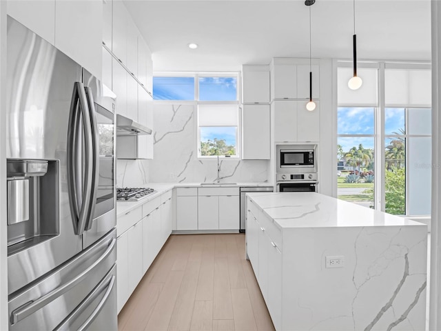 kitchen with pendant lighting, sink, backsplash, stainless steel appliances, and white cabinets