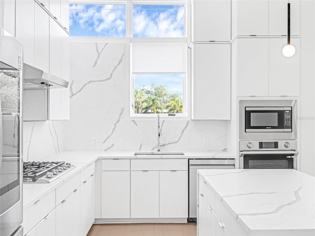 kitchen featuring appliances with stainless steel finishes, decorative light fixtures, tasteful backsplash, white cabinetry, and sink