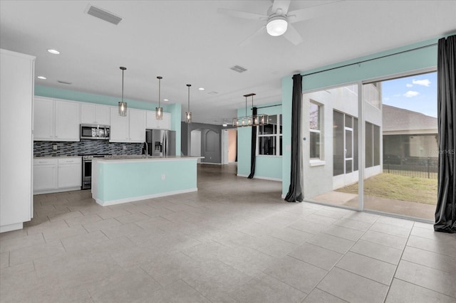 kitchen with decorative light fixtures, an island with sink, white cabinets, backsplash, and stainless steel appliances