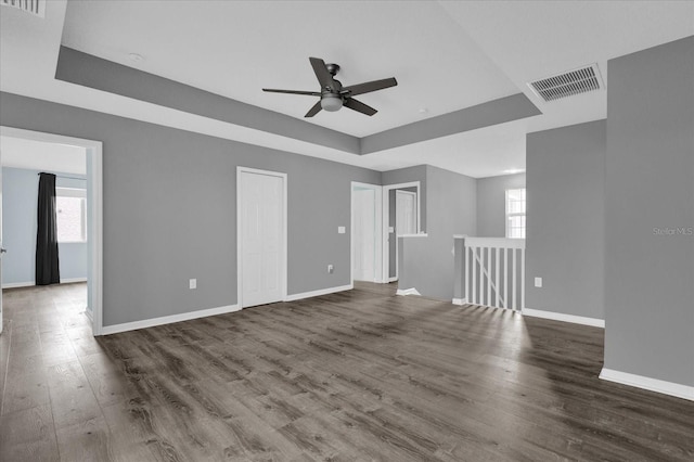 unfurnished living room with dark hardwood / wood-style floors, ceiling fan, a healthy amount of sunlight, and a tray ceiling