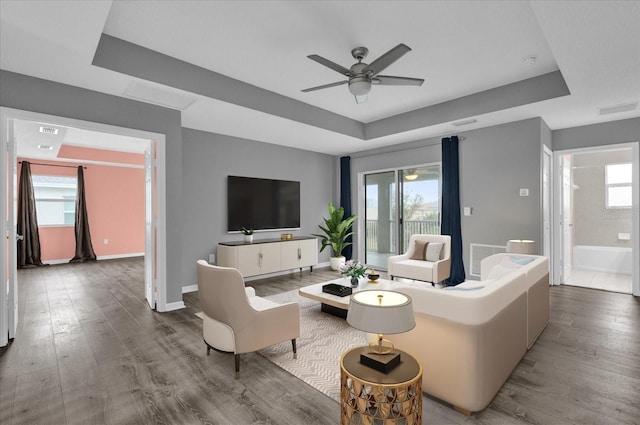 living room with hardwood / wood-style flooring, a raised ceiling, and ceiling fan