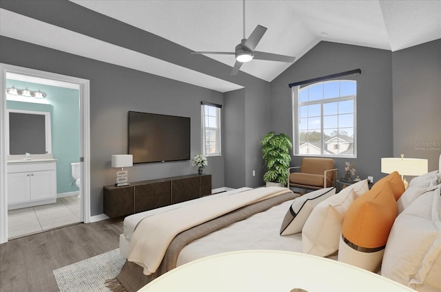 bedroom featuring multiple windows, vaulted ceiling, ensuite bathroom, and light wood-type flooring