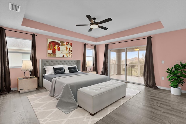 bedroom featuring ceiling fan, wood-type flooring, access to exterior, and a raised ceiling