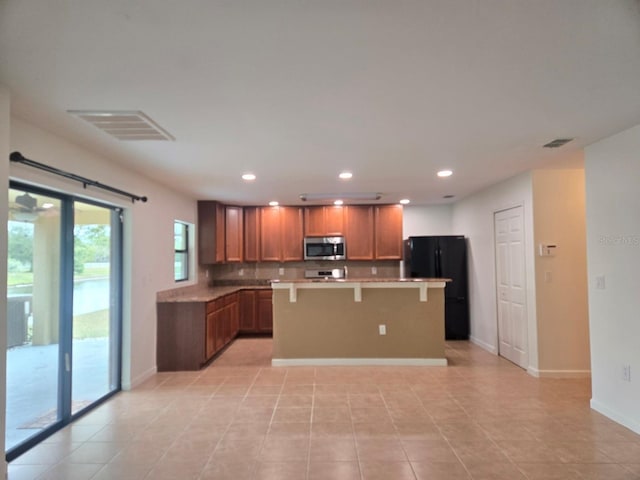 kitchen with black fridge, a center island, light tile patterned floors, a kitchen breakfast bar, and backsplash