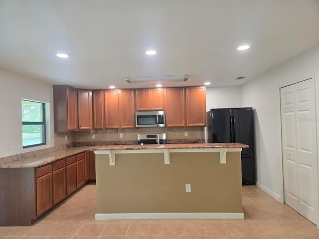 kitchen with a kitchen bar, light stone counters, a center island, appliances with stainless steel finishes, and decorative backsplash