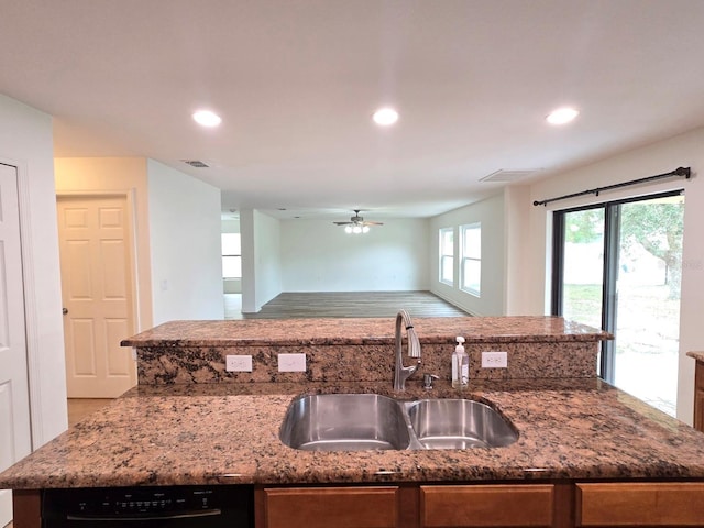 kitchen with light stone counters, a kitchen island with sink, and sink