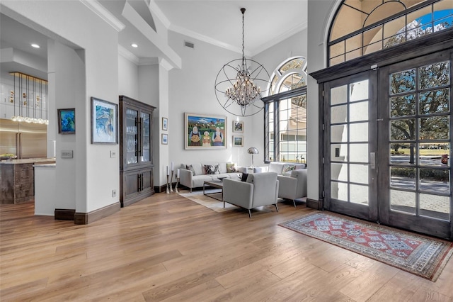 foyer with a towering ceiling, french doors, ornamental molding, a notable chandelier, and light hardwood / wood-style flooring