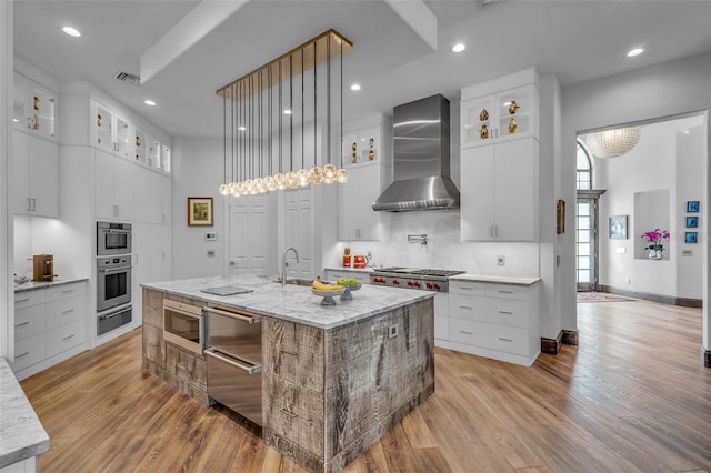 kitchen featuring a spacious island, white cabinets, light stone countertops, and wall chimney range hood