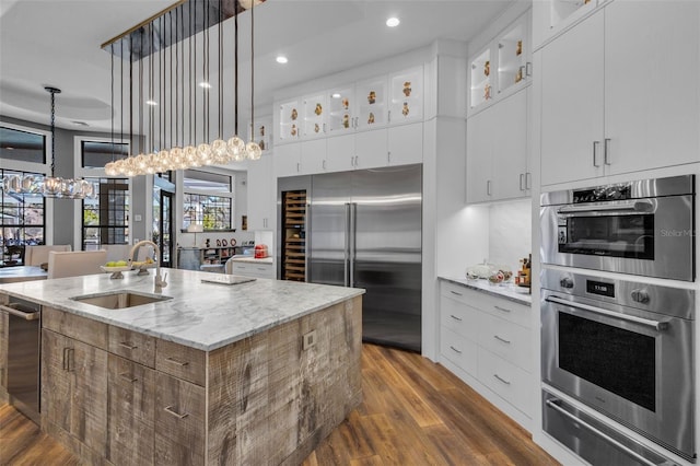 kitchen with sink, white cabinetry, appliances with stainless steel finishes, light stone countertops, and a kitchen island with sink