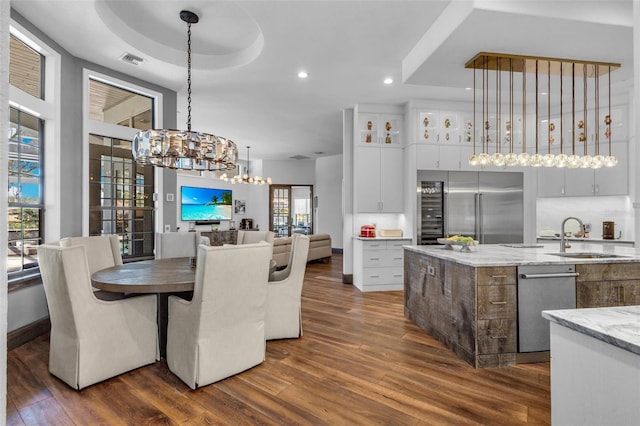 kitchen with appliances with stainless steel finishes, white cabinetry, sink, hanging light fixtures, and light stone countertops