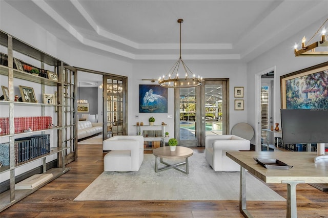 living area with dark wood-type flooring, an inviting chandelier, and a tray ceiling